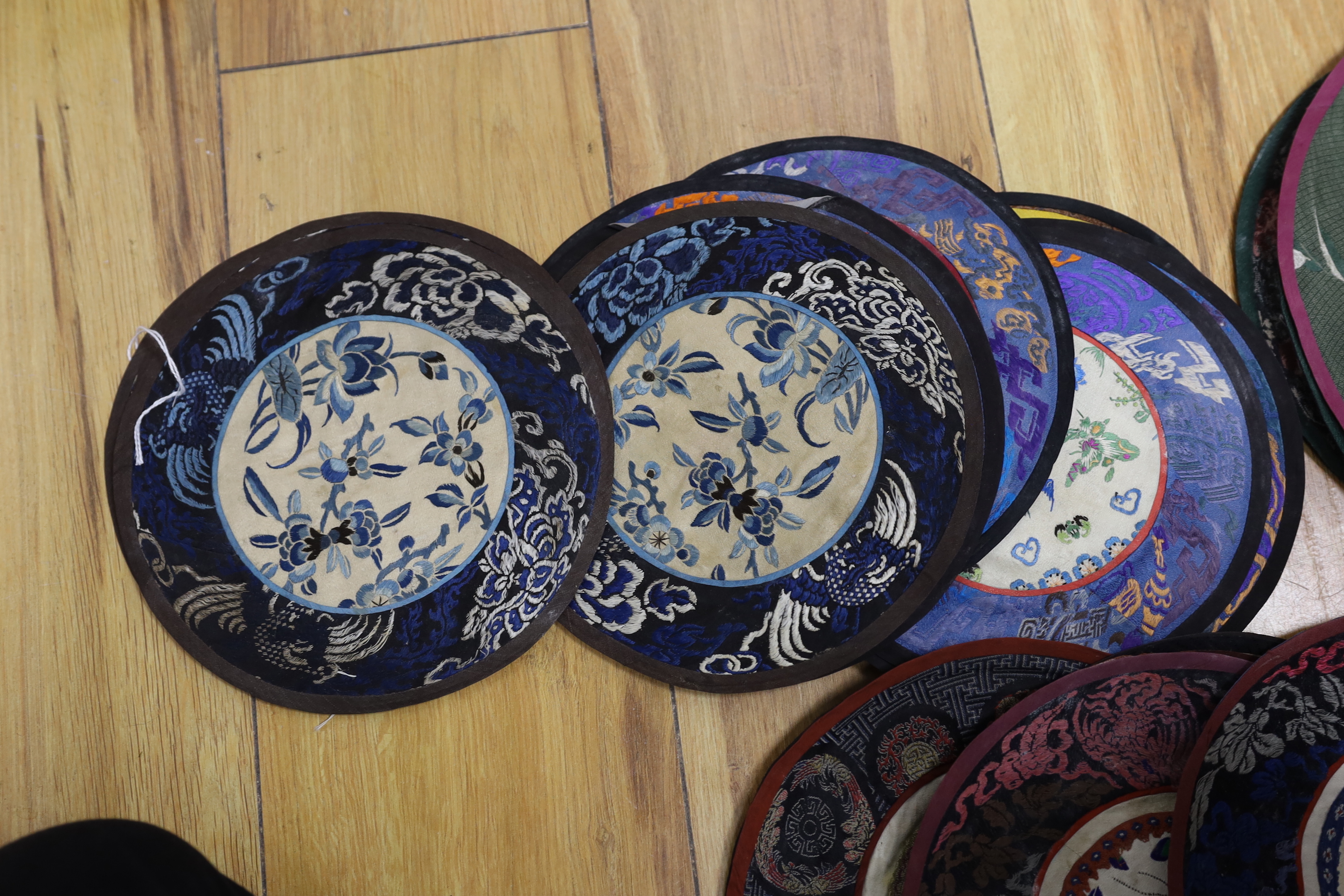 Forty two Chinese embroidered circular mats with damask borders, largest 25cm in diameter